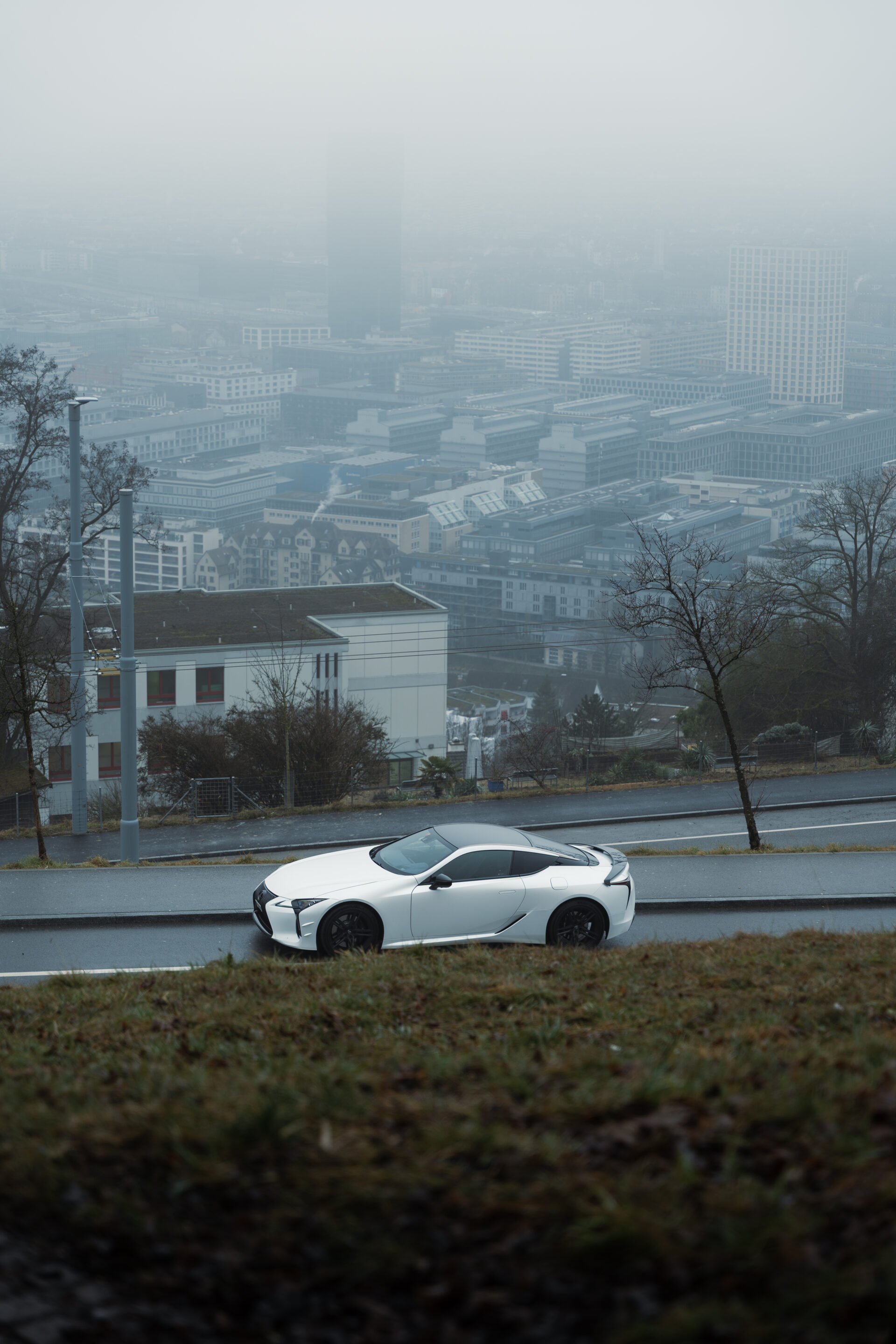 A foggy day in Zurich, Switzerland with a Lexus LC500 Ultimate Edition in the foreground being parked on a random street and showing off the city skyline